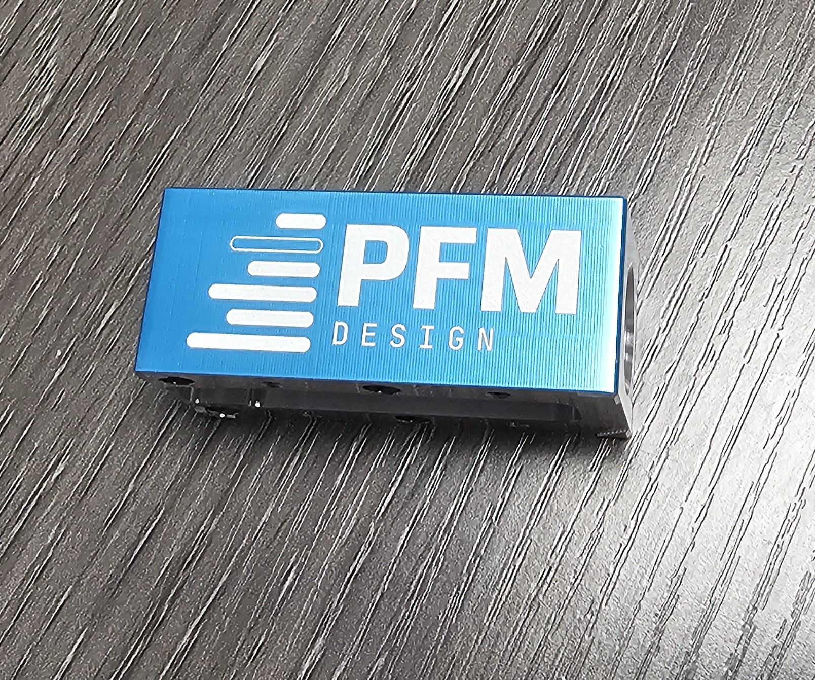 Etched PFM Design logo on anodized blue aluminum block